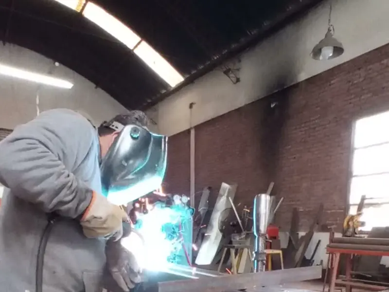 Soldador trabajando una pieza metálica dentro del taller
