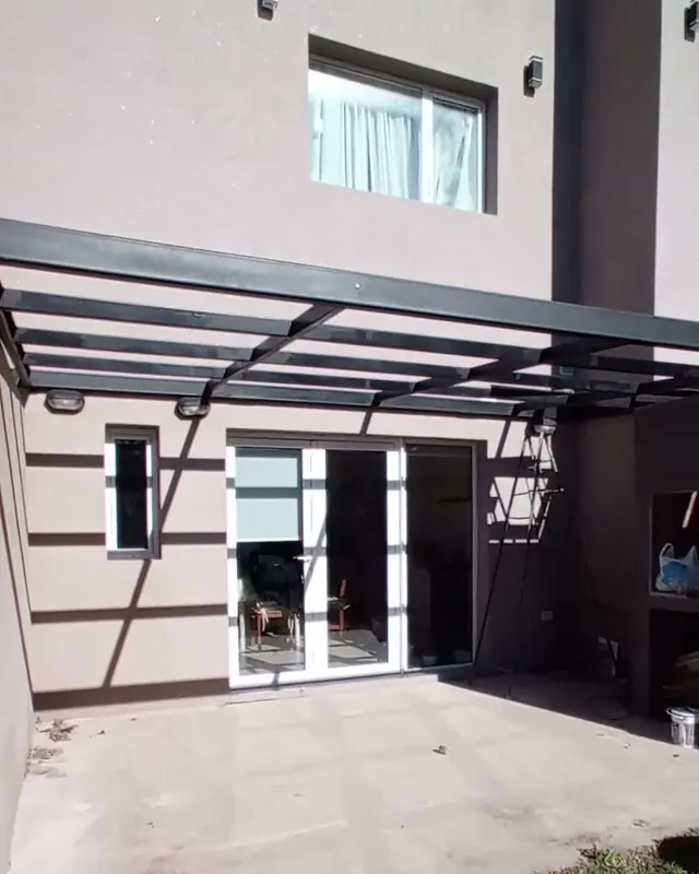 Pérgola metálica sobre el patio de una casa de dos plantas